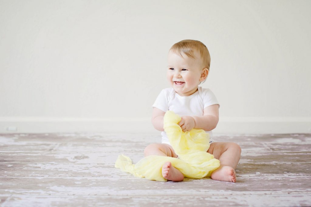 A baby sitting wearing white laughs at something in the distance